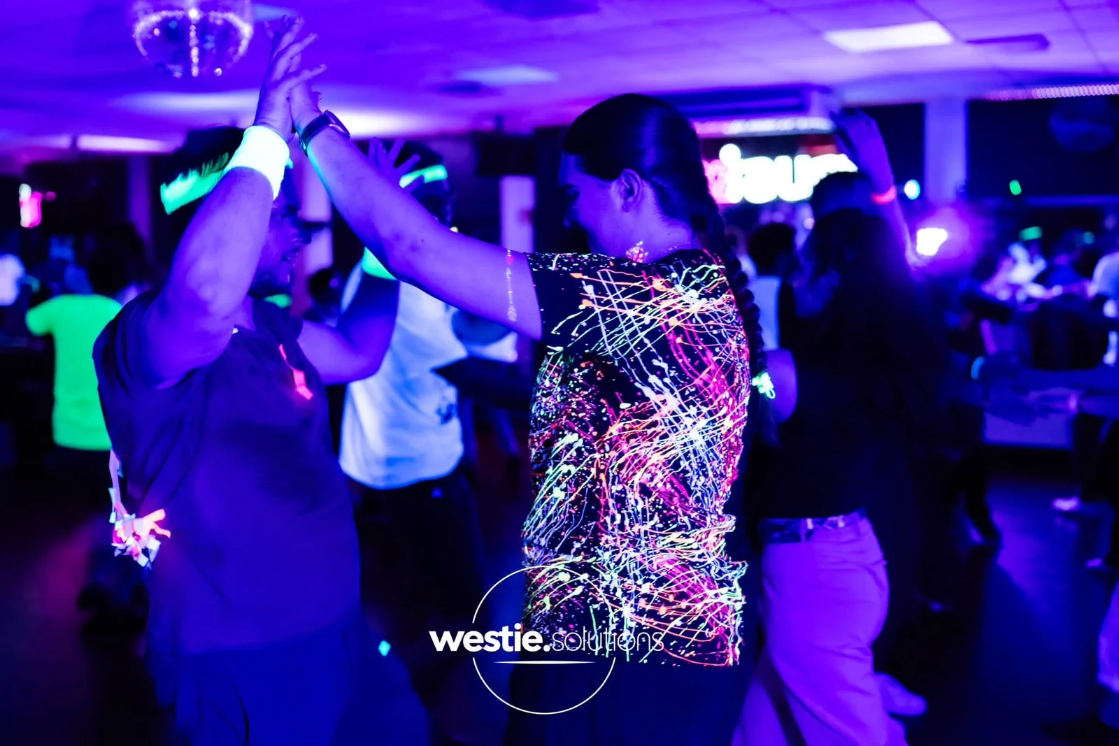 Tanzende bei der Neon-Party mit leuchtenden Kleidungsdetails unter UV-Licht
